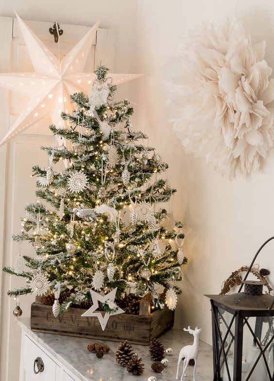 a charming vintage tabletop Christmas tree with lights, white and silver ornaments, lacey snowflakes and lots of pinecones in the crate