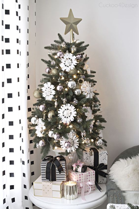 a chic and shiny tabletop Christmas tree with lights, silver and gold glitter ornaments, white paper snowflakes and a star topper