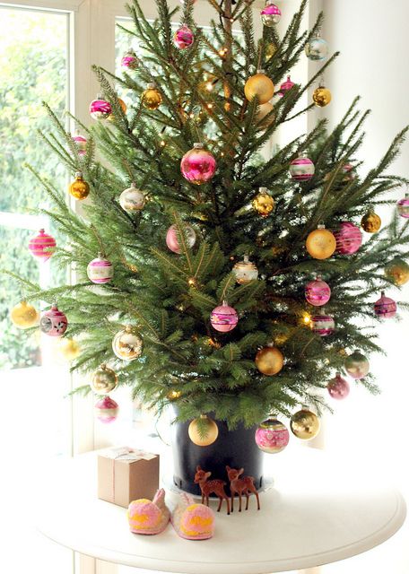 a colorful tabletop Christmas tree decorated with pink and yellow ornaments and nothing else is modern and bold