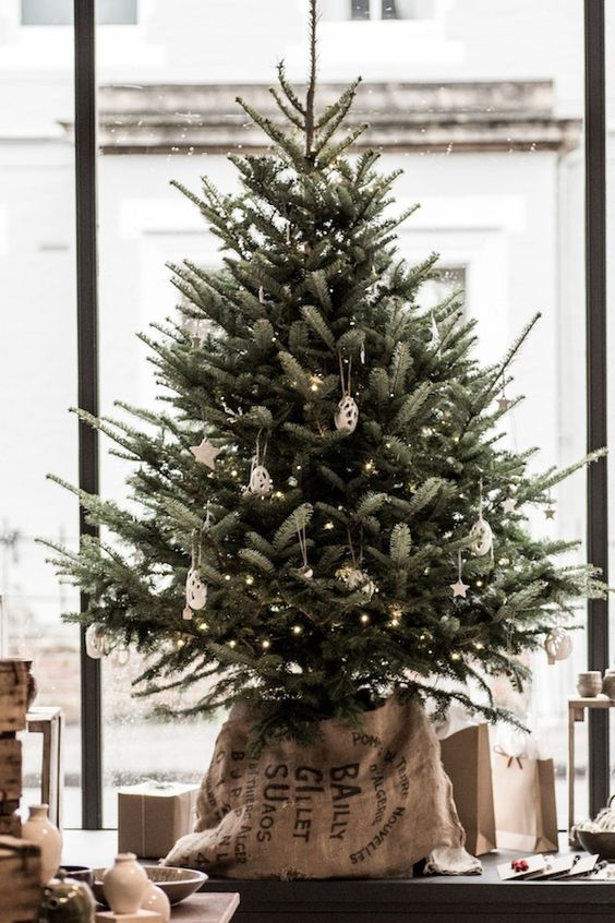 a delicate tabletop Christmas tree decorated with lights, white clay ornaments and put into a sack for a slight industrial feel