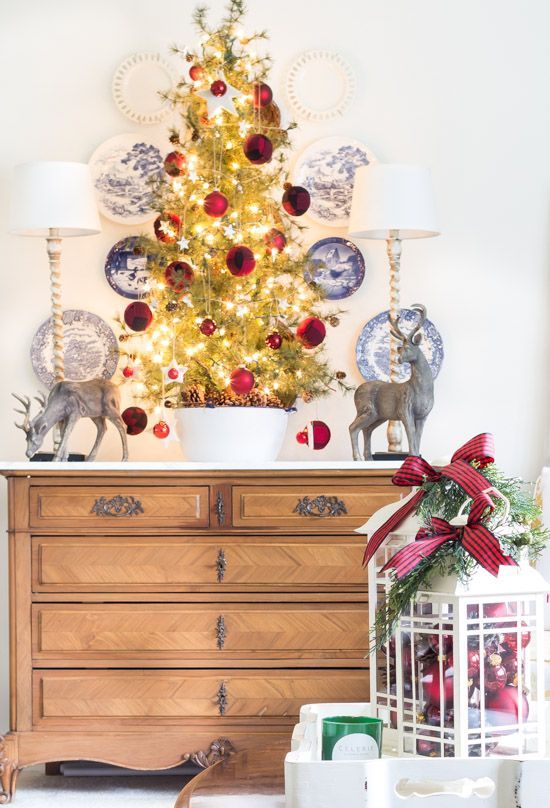 a lovely tabletop Christmas tree with lights, tiny star and large red ornaments and pinecones in the bowl is amazing