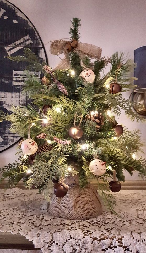 a rustic vintage tabletop Christmas tree with lights, large bells, snowman ornaments, burlap bows and garlands