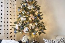 a vintage-inspired tabletop Christmas tree with blue and silver ornaments, wooden bead garlands, lights and paper snowflakes put into a silver pot