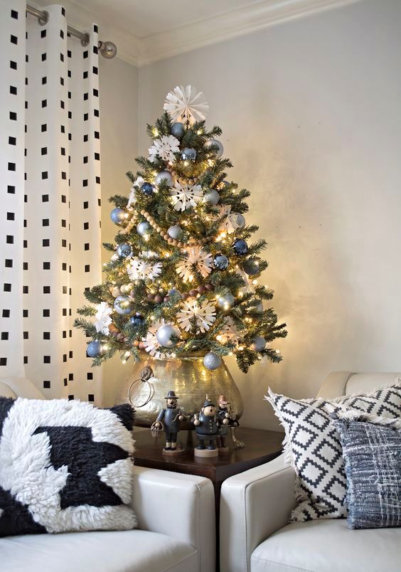a vintage inspired tabletop Christmas tree with blue and silver ornaments, wooden bead garlands, lights and paper snowflakes put into a silver pot
