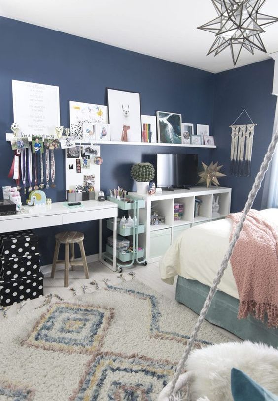 a lovely teen room with navy walls, a turquoise bed, neutral and pastel bedding, a white desk or makeup vanity, a storage unit and a ledge gallery wlal