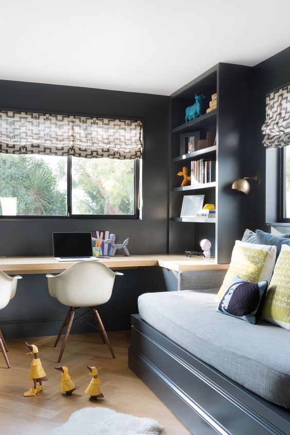 a moody teen bedroom with a bed, a built-in desk and a storage unit, a couple of chairs and printed textiles