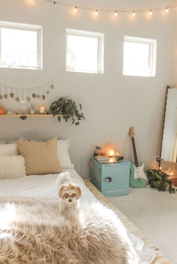 a neutral teen bedroom with neutral walls, a pallet bed, a floor mirror, a blue storage cabinet, a floating shelf with greenery and candles and a guitar