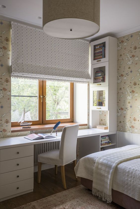 a neutral teen room with printed map wallpaper, a built-in desk with storage units, a bed with neutral bedding and a curtain