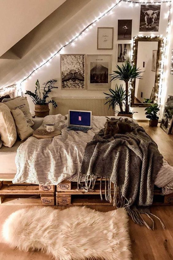 an attic teen room with a pallet bed with pretty bedding, a black and white gallery wall, a mirror and lots of lights and potted greenery