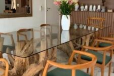 a beautiful dining table with pieces of driftwood holding the glass tabletop, green and stained chairs and a gold chandelier