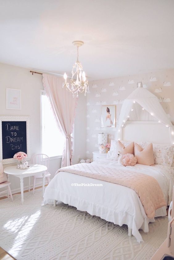 a blush flamingo printed wallpaper wall, a white bed with a lit up cnaopy, pink and white bedding, vintage dinign set and a crystal chandelier