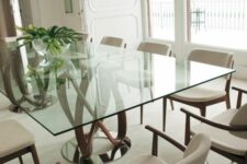 a catchy dining table with a glass tabletop and a rich-stained swirl base plus upholstered chairs and a lovely view for a perfect dining room