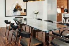 a chic modern table with stained wooden legs and a glass top, marching chairs with leather upholstery and black and gold pendant lamps