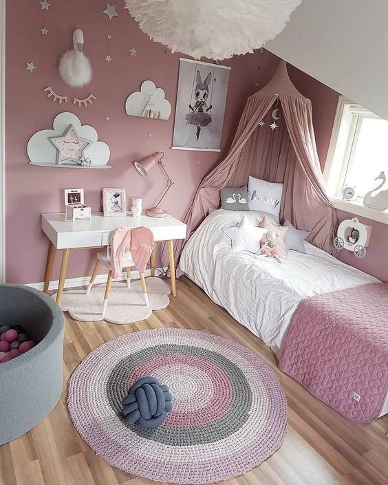 a dusty pink girl's bedroom, with a bed with dusty pink bedding and a canopy, a striped rug, a gallery wall and some star-shaped pillows