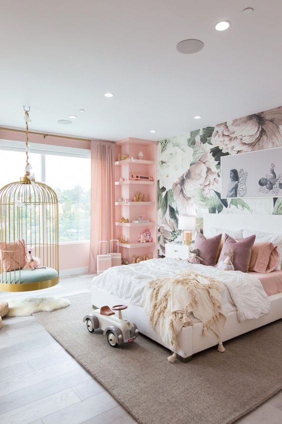 a fantastic girl's bedroom with a floral accent wall, a pink wall with built-in shelves, a white bed with pink bedding, a cage pendant chair