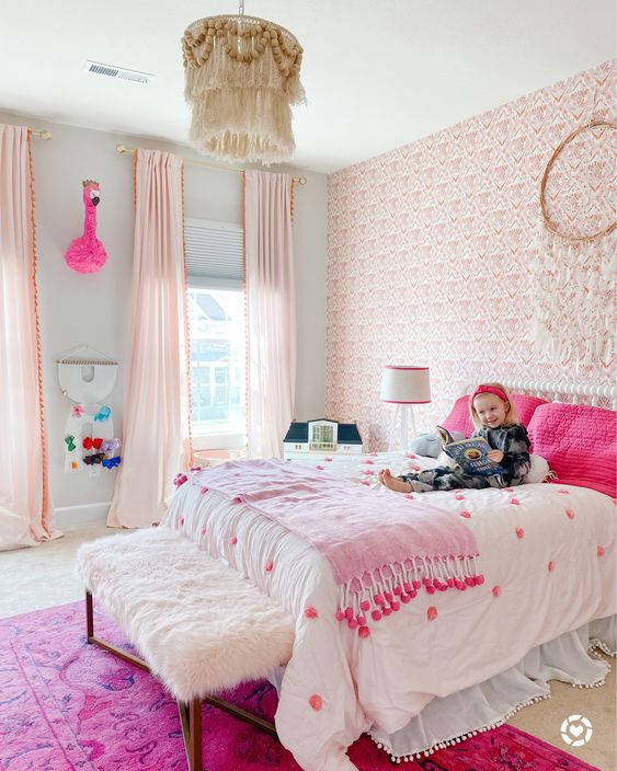 a fantastic pink boho girl's bedroom with a pink wallpaper wall, light pink curtains, a bed with hot pink pillows and a hot pink rug