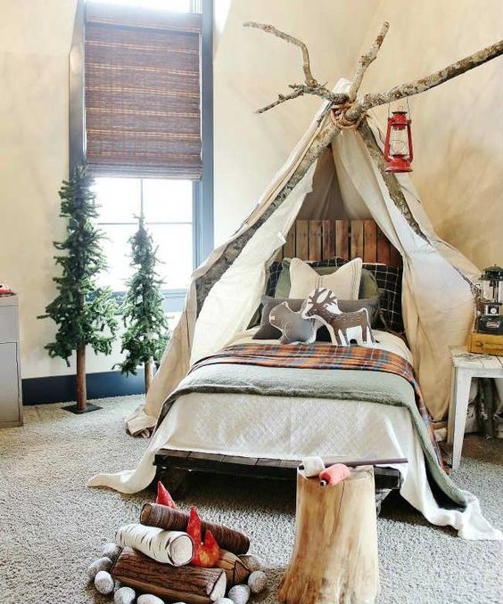 a gorgeous camp-themed kids' room with canopy on branches, woven shades, faux trees and a faux fireplace