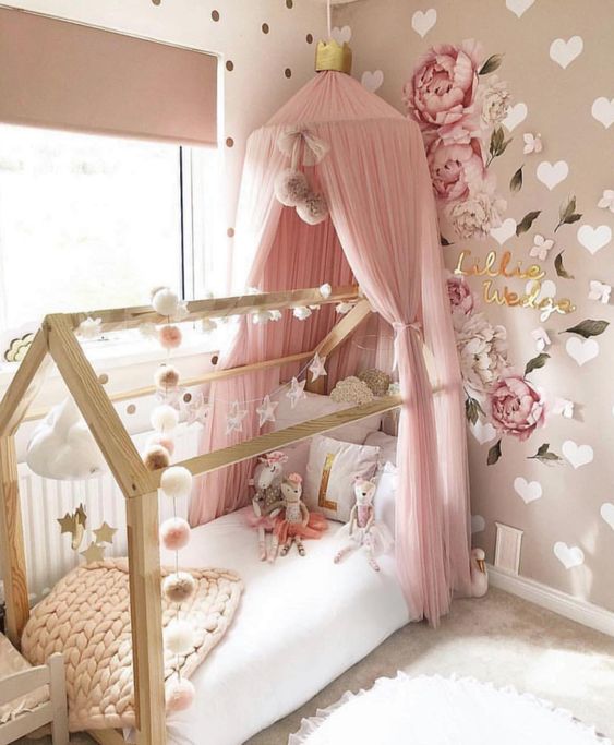 a gorgeous girl's bedroom with tan and white walls with hearts and polka dots, a bed with a pink canopy, garlands and paitned blooms