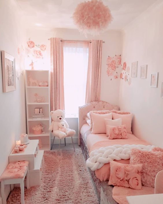 a pink and white girl's bedroom with an upholstered bed with pink bedding, pink curtains, a fluffy lamp, a white shelving unit and gallery walls