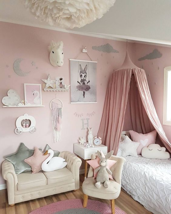a pink girl's bedroom with a pink accent wall, neutral furniture, neutral bedding, a pink canopy, a gallery wall and a fluffy pendant lamp