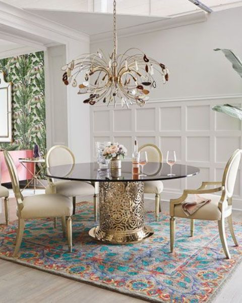 a refined and chic dining table with a catchy floral gold base and a smoked glass tabletop and a crystal chandelier that echoes with the table
