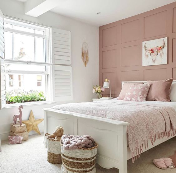 a relaxed and delicate girl's room with a dusty pink wall, a white bed with dusty pink bedding, artwork and pillows is cute