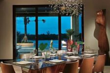 a sophisticated dining room with a glass top dining table and a bamboo base, chic upholstered chairs and a large bubble chandelier over the space