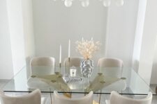 a sophisticated dining room with a large polished gold base and a glass tabletop, creamy chairs and a mid-century modern chandelier