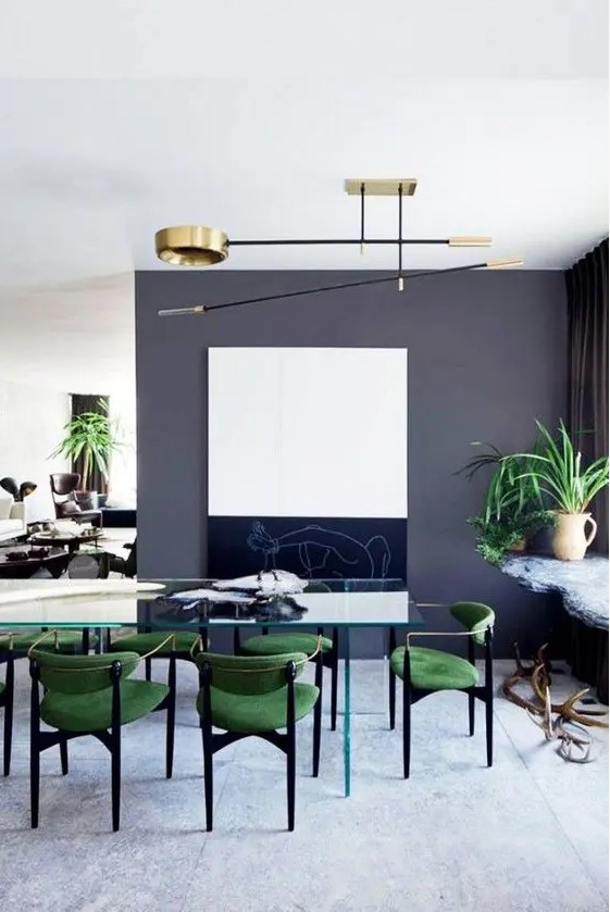 an all-glass dining table with bold emerald chairs on black legs looks chic and interesting