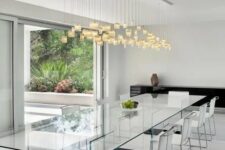an ethereal all-glass dining table with dark bases and neutral chairs, a pendant lighting fixture to accentuate the space