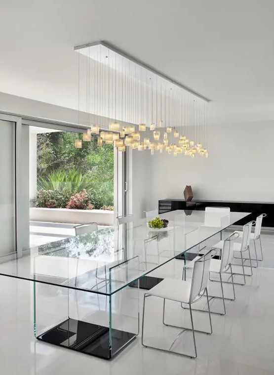 an ethereal all-glass dining table with dark bases and neutral chairs, a pendant lighting fixture to accentuate the space