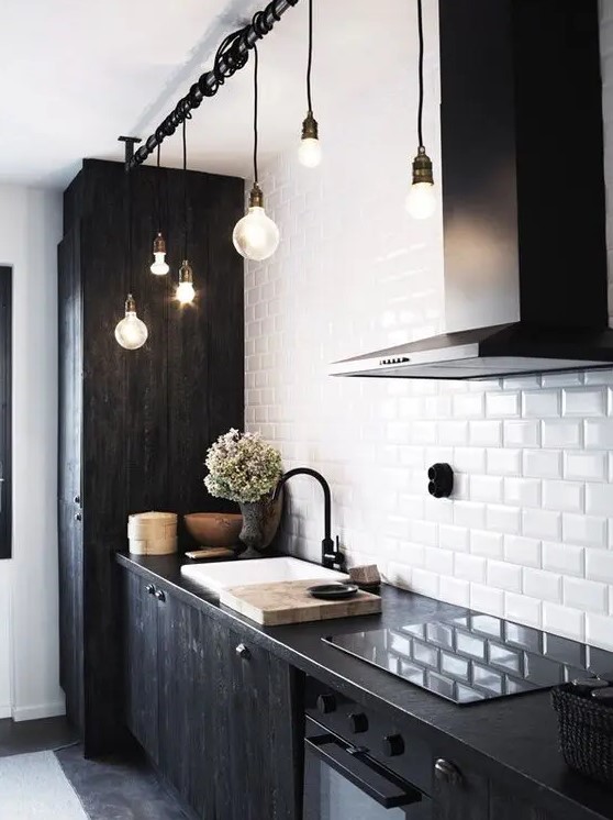 a bold kitchen with black wood cabinets, a white subway tile kitchen backsplash, black countertops and black pendant bulbs