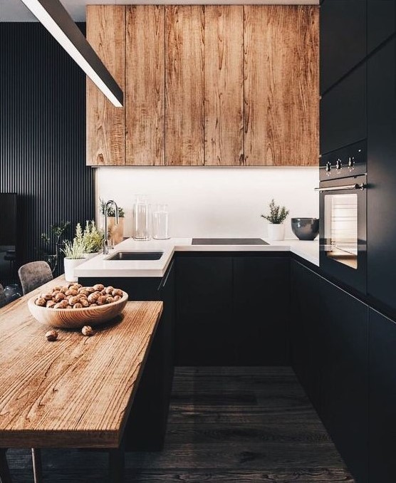 a chic black kitchen with a wooden table and a large hood plus white countertops looks very stylish and bold
