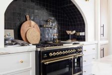 a chic vintage kitchen with white shaker cabinets, black Zellige tiles, a vintage black cooker and gold fixtures and touches