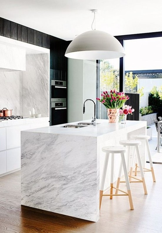 a chic white kitchen with white stone countertops and a backsplash and a waterfall coutnertop on the kitchen island