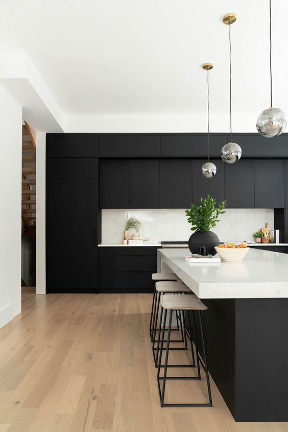 a contemporary black and white kitchen with matte cabinets, white countertops and a backsplash and bubble lamps