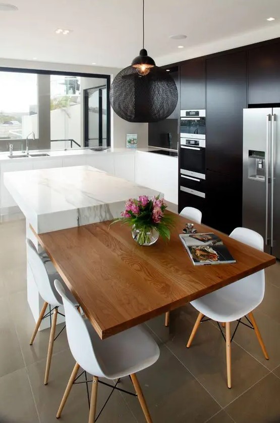 a contemporary contrasting kitchen with black and white cabinets, a white stone kitchen island with an additional countertop, a black pendant lamp