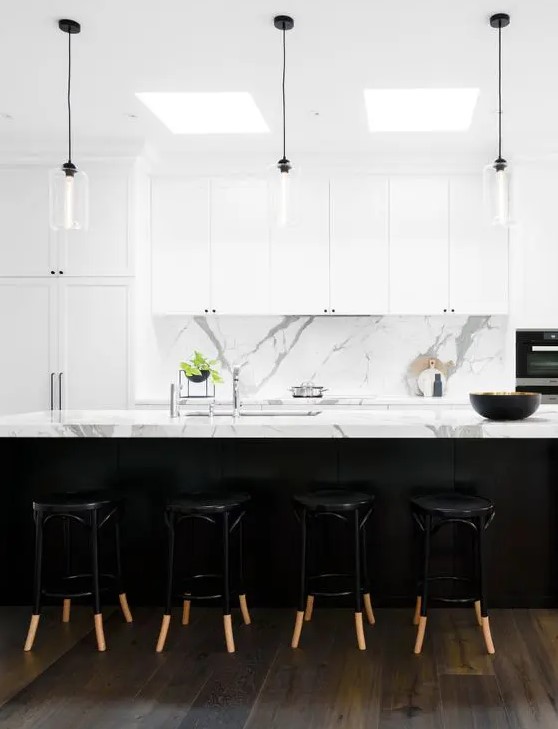 a contemporary kitchen featuring white marble benchtops and splashback, white shaker cabinets with minimal black handles, glass pendant lights with black cords