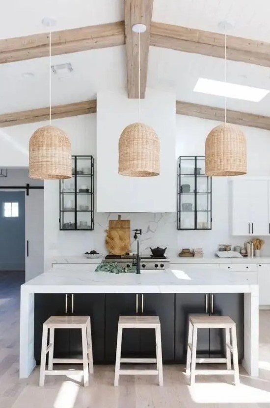 a contemporary kitchen in white, with cabinets with black knobs, a large hood, a black kitchen island with a white countertop and woven pendant lamps