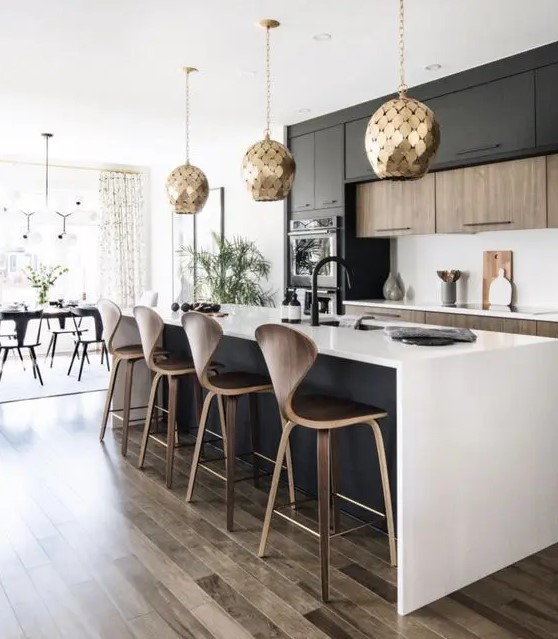 a contemporary kitchen with stained and black cabinets, a black kitchen island, white countertops and a backsplash, gold scale pendant lamps