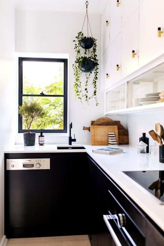 a contrasting kitchen with white upper and black lower cabinets, white countertops and black fixtures plus greenery in pots