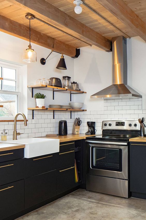 a farmhouse black and white kitchen with matte cabinets, butcherblock countertops, wooden shelves and a ceiling, a shiny metal hood