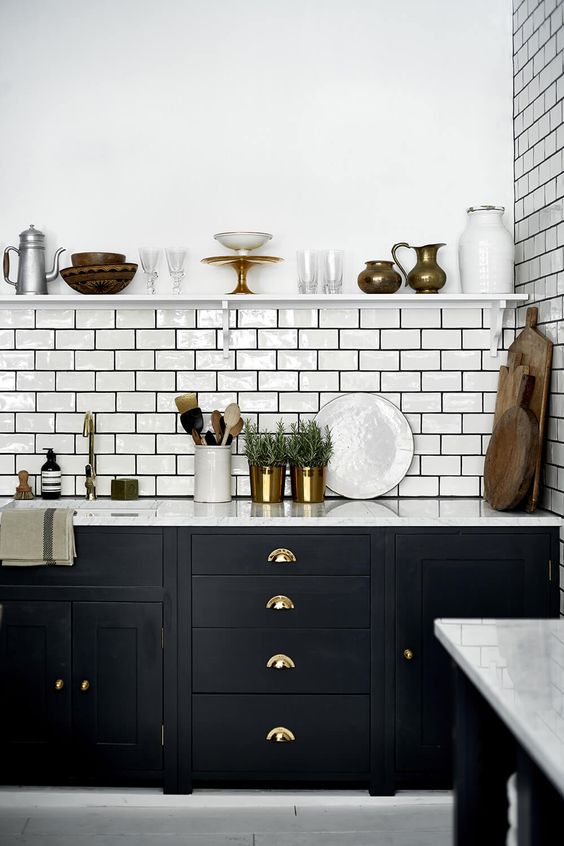 a lovely mid-century modern kitchen with black cabinets, white stone countertops, a white subway tile backsplash and black grout