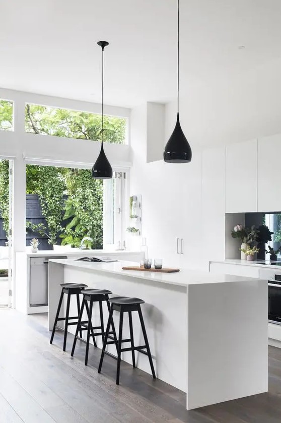 a miniamlist white kitchen with several black accents like a backsplash and pendant lamps, stools and fixtures looks airy and bright