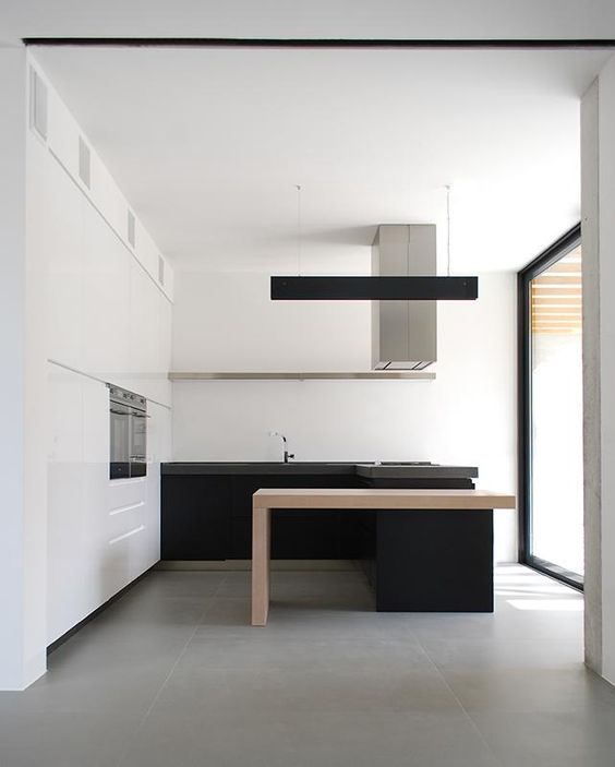 a minimalist black and white kitchen with a white storage unit and upper cabinets, black lower ones and a kitchen island with a light-stained table