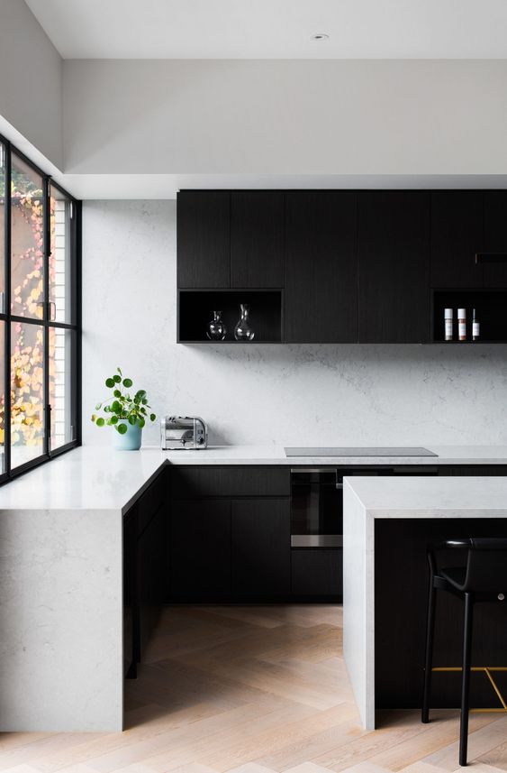 a minimalist black and white kitchen with matte black cabinets, white stone countertops and a backsplash, black stools is a chic space to be