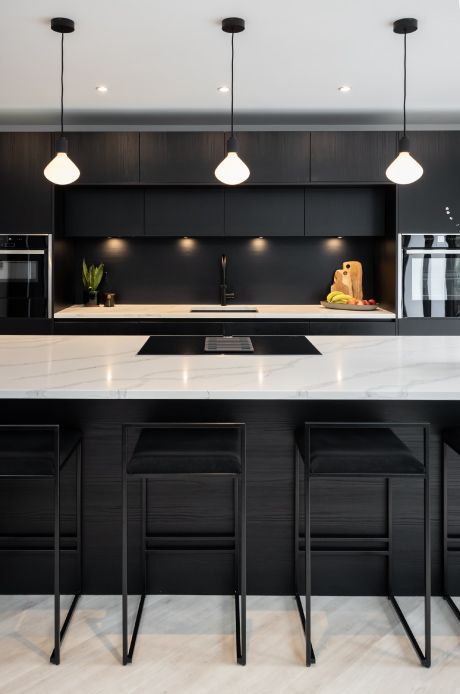 a minimalist kitchen with matte black cabinets, white stone countertops, black stools and pendant lamps and built-in lights