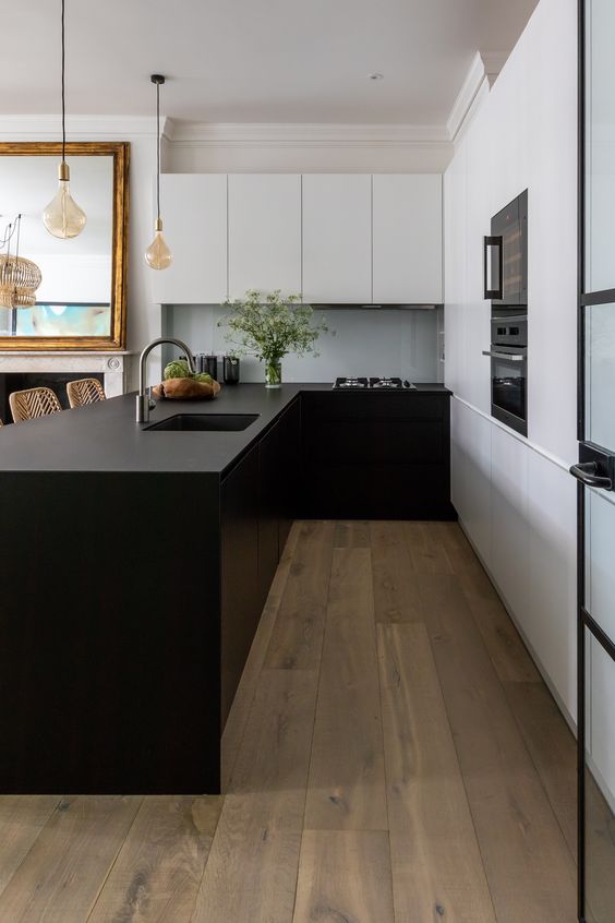 a minimalist kitchen with matte wihte and black cabinets, a large kitchen island, black built-in appliances and pendant lamps