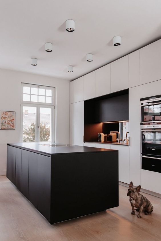 a minimalist kitchen with white cabinets and a black kitchen island, a black additional cabinet and a mirror backsplash, white lamps