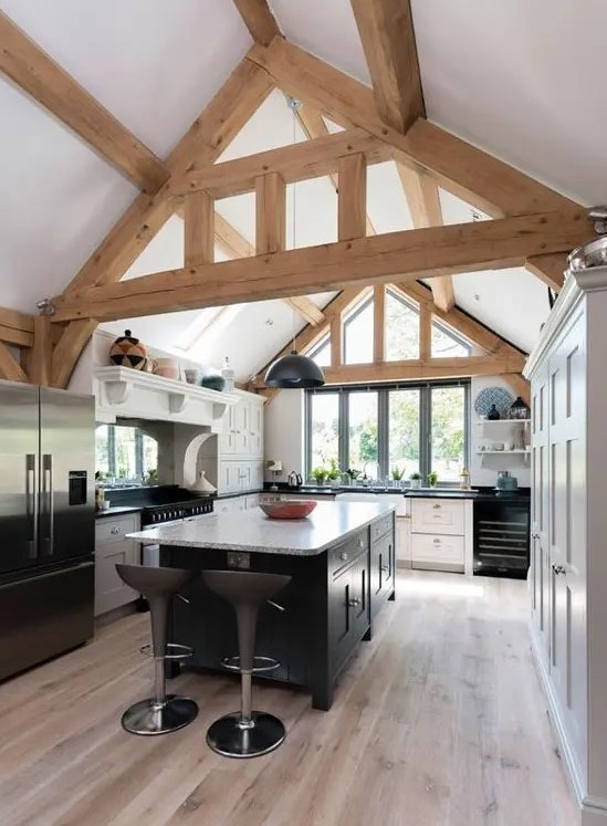 a modern barn kitchen with wooden beams, white cabinets and a black kitchen island plus black appliances looks cool and fresh